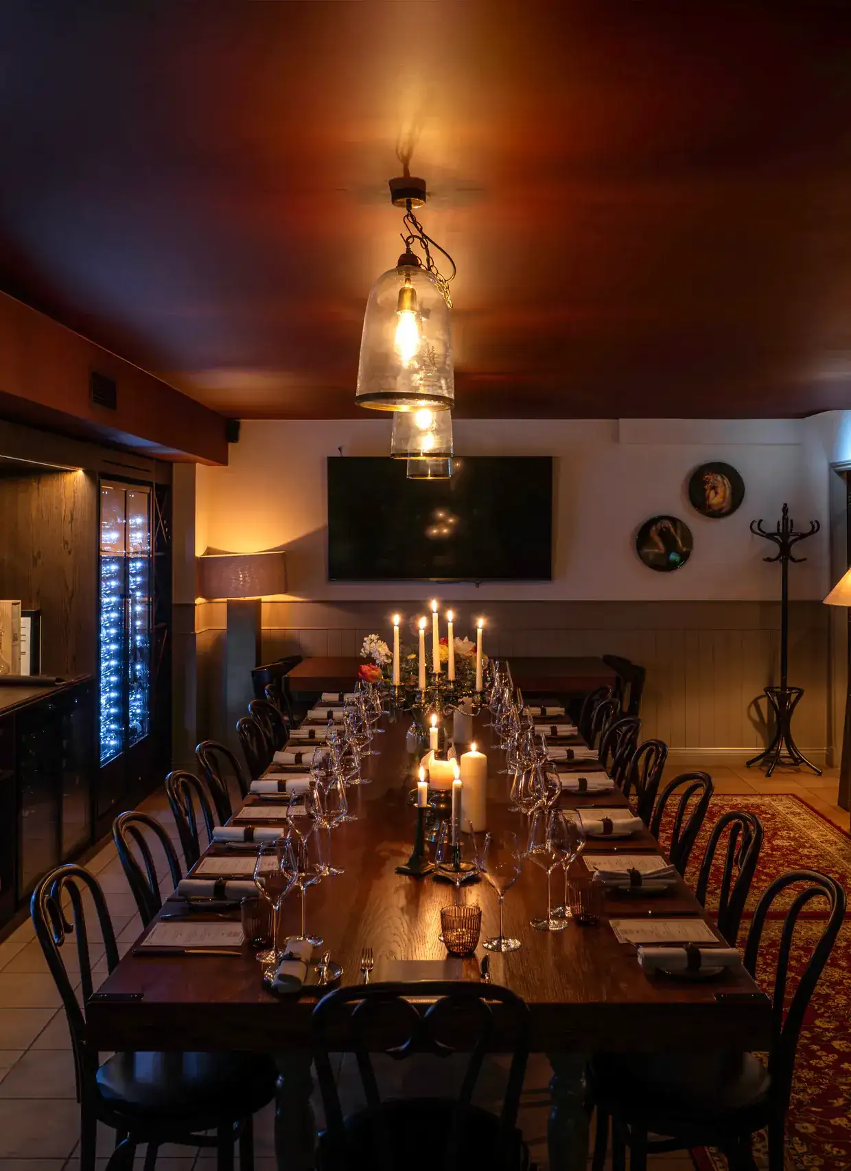 The private dining room at Vinoly laid for dinner: a long candlelit table under glass pendant lamps, with lit wine fridges along the wall